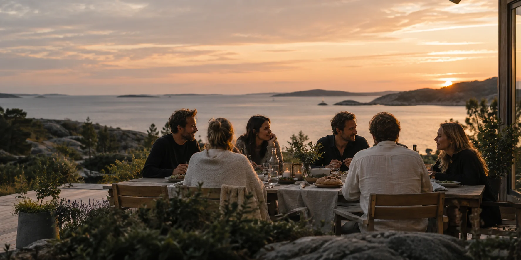 Venner rundt et langbord ved sjøen i solnedgangen
